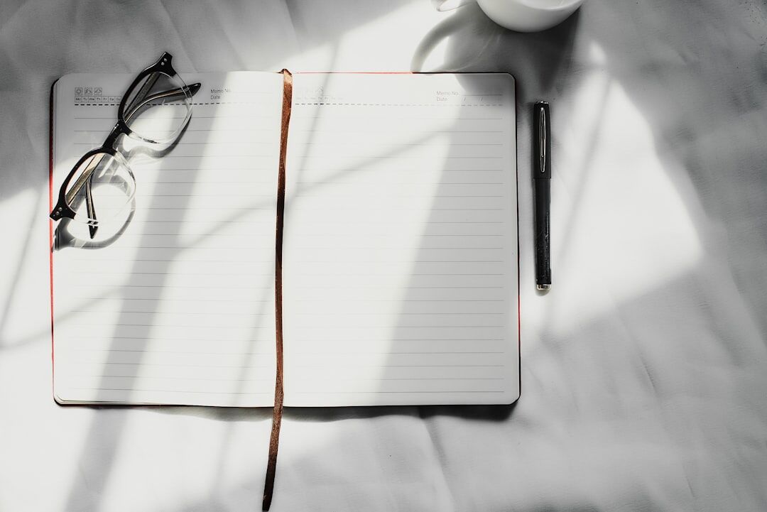 Open notebook, pen and eyeglasses on a wooden table in soft light